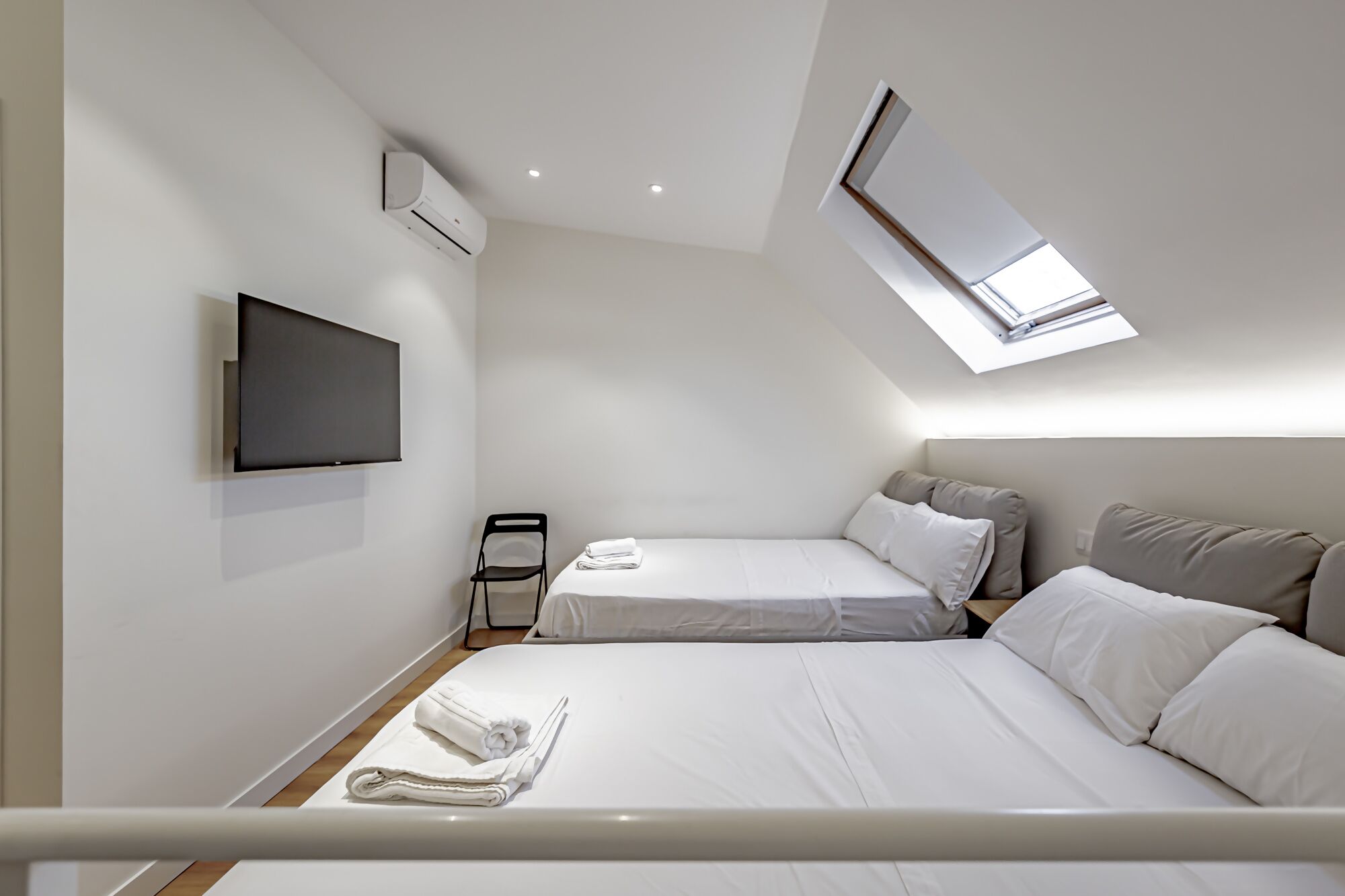 Een moderne hotelkamer met een flatscreen televisie, een bed, een stoel en een dakraam.