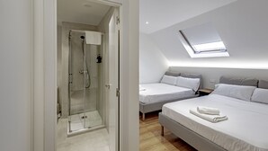 A modern bedroom with a skylight, a shower, two beds, and a bedside table.