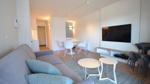 A modern living room with a grey sofa, a small round table, and a flat-screen TV mounted on the wall. - Coastal Retreat with Terrace (Oostduinkerke)
