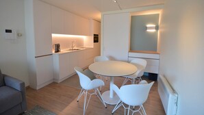 A modern kitchen with white cabinetry, a round dining table with white chairs, and a built-in oven. - Coastal Retreat with Terrace (Oostduinkerke)