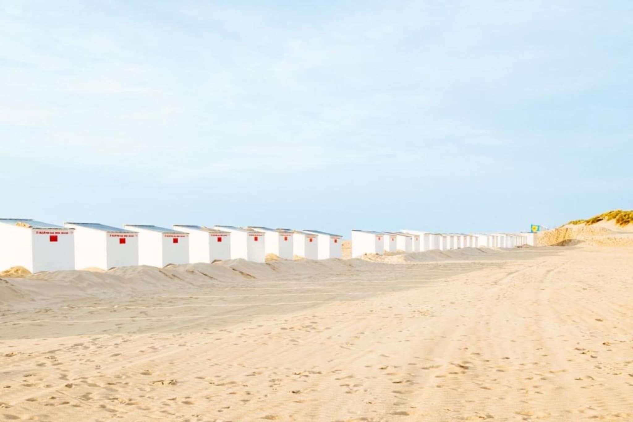 A row of white beach huts with red signage, arranged along a sandy beach.