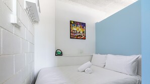 A neatly made bed with white linens, a colorful abstract painting on the wall, and a small clock on a shelf. - In the Heart of the City – Quaint Studio in the Prime Location! (Melbourne)