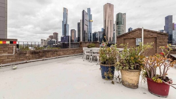 A rooftop terrace with potted plants, a brick wall, and a city skyline in the background. - In the Heart of the City – Quaint Studio in the Prime Location! (Melbourne)