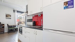 A modern kitchen with white cabinets, a red backsplash, and a built-in oven. There is a dining area with a table and chairs, and a window providing natural light. - In the Heart of the City – Quaint Studio in the Prime Location! (Melbourne)