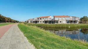 A row of modern apartment buildings with balconies, a paved walkway, and a body of water in the foreground. - Apartment by the Beach with Stunning Dunes (Julianadorp aan Zee)