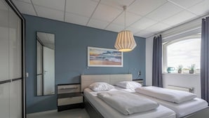 A modern bedroom with a large bed, a bedside table, a mirror, and a window with curtains. - Apartment by the Beach with Stunning Dunes (Julianadorp aan Zee)