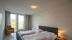 Hotelkamer met twee bedden, een stoel, nachtkastje en uitzicht door een groot raam.