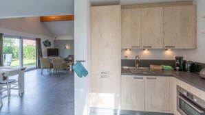 A modern kitchen with light wood cabinets, a built-in oven, and a dining area with a table and chairs.