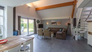 A spacious living area with a wooden ceiling, a sofa, a coffee table, and a dining table with chairs.