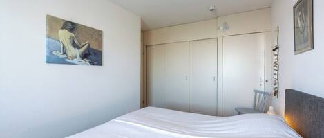 Ein Schlafzimmer mit einem Bett, einem Kleiderschrank, einem Sessel und einem Bild an der Wand.