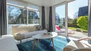 En moderne stue med sofa, sofabord og en stor skydedør, der fører ud til en udendørs terrasse.