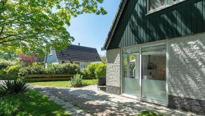 Et moderne hus med stenvæg og store glasdøre, omgivet af en velplejet have og en belagt indkørsel.
