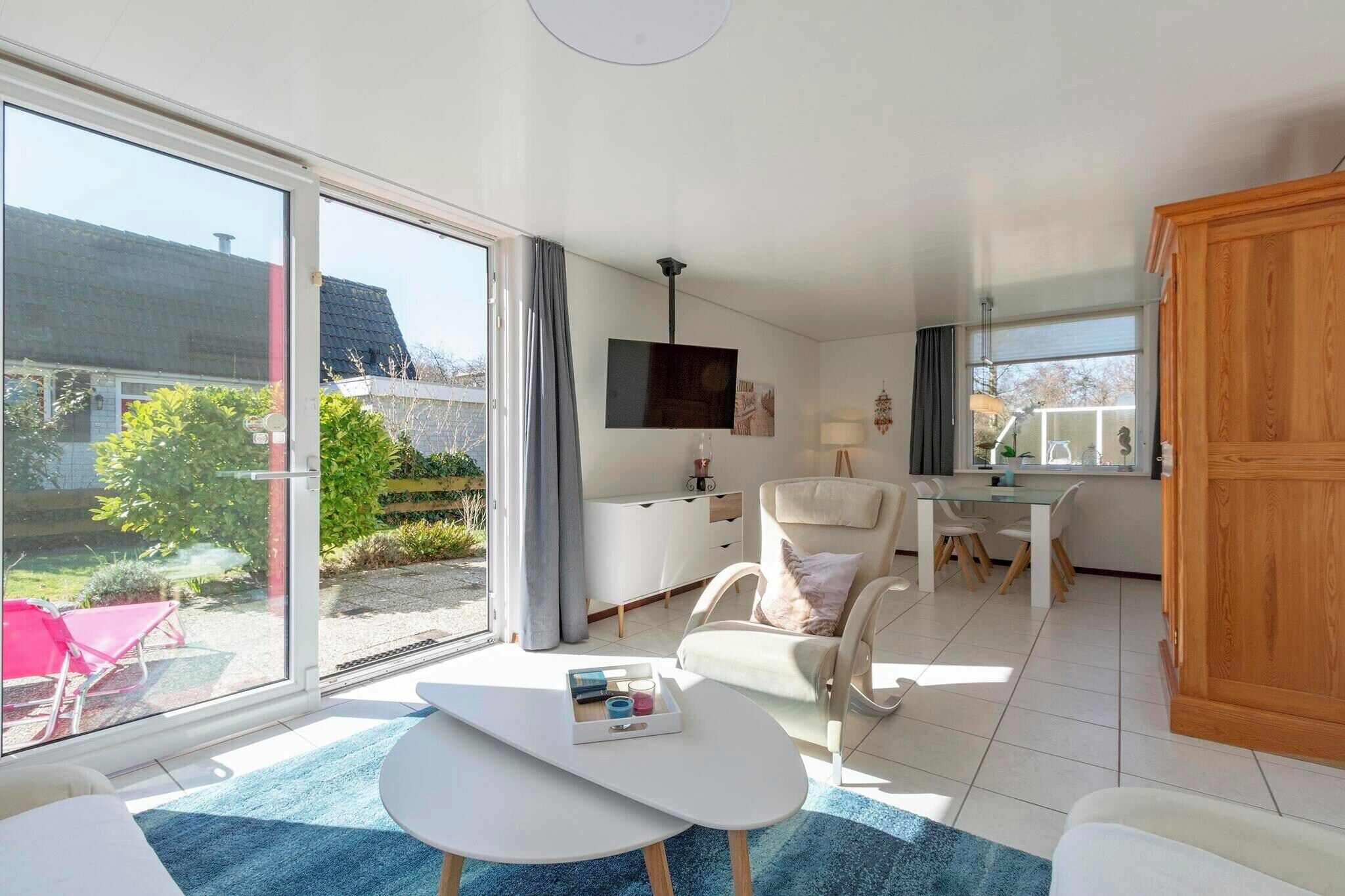 A spacious living area with a large sliding glass door leading to a garden, a white sofa, a small white table, and a wooden cabinet.