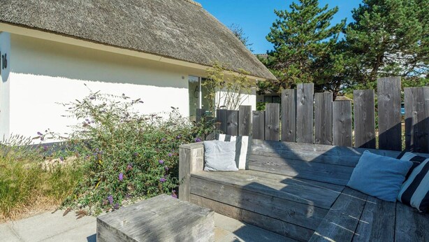 A wooden deck with a thatched roof house, a wooden fence, and a bench with cushions.
