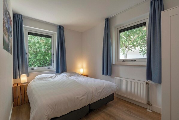 A bedroom with a bed, two windows with curtains, a bedside lamp, and a radiator.