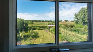 Ein Fenster mit Blick auf eine grüne Landschaft, darunter Felder und ein kleines Gebäude.