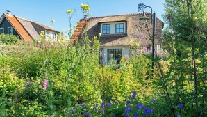 Ein traditionelles Haus mit einem Strohdach, umgeben von üppiger Vegetation und Wildblumen.