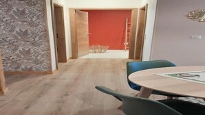 Ein Zimmer mit Holzboden, einem runden Tisch mit Stühlen, einer roten Tür und einer Wand mit Muster.