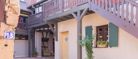 A traditional European-style building with a wooden balcony, a door, and potted plants.