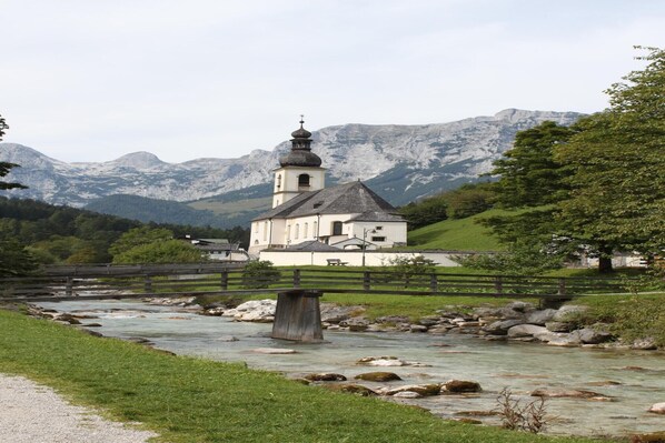 Una iglesia con un campanario, un río y montañas al fondo.