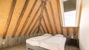 A bedroom with a sloped ceiling, a bed, a bedside table, and a window. - Vossehoeck 3 Apartment with nature reserve view (Callantsoog)