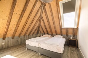 A bedroom with a sloped ceiling, a bed, a bedside table, and a window. - Vossehoeck 3 Apartment with nature reserve view (Callantsoog)
