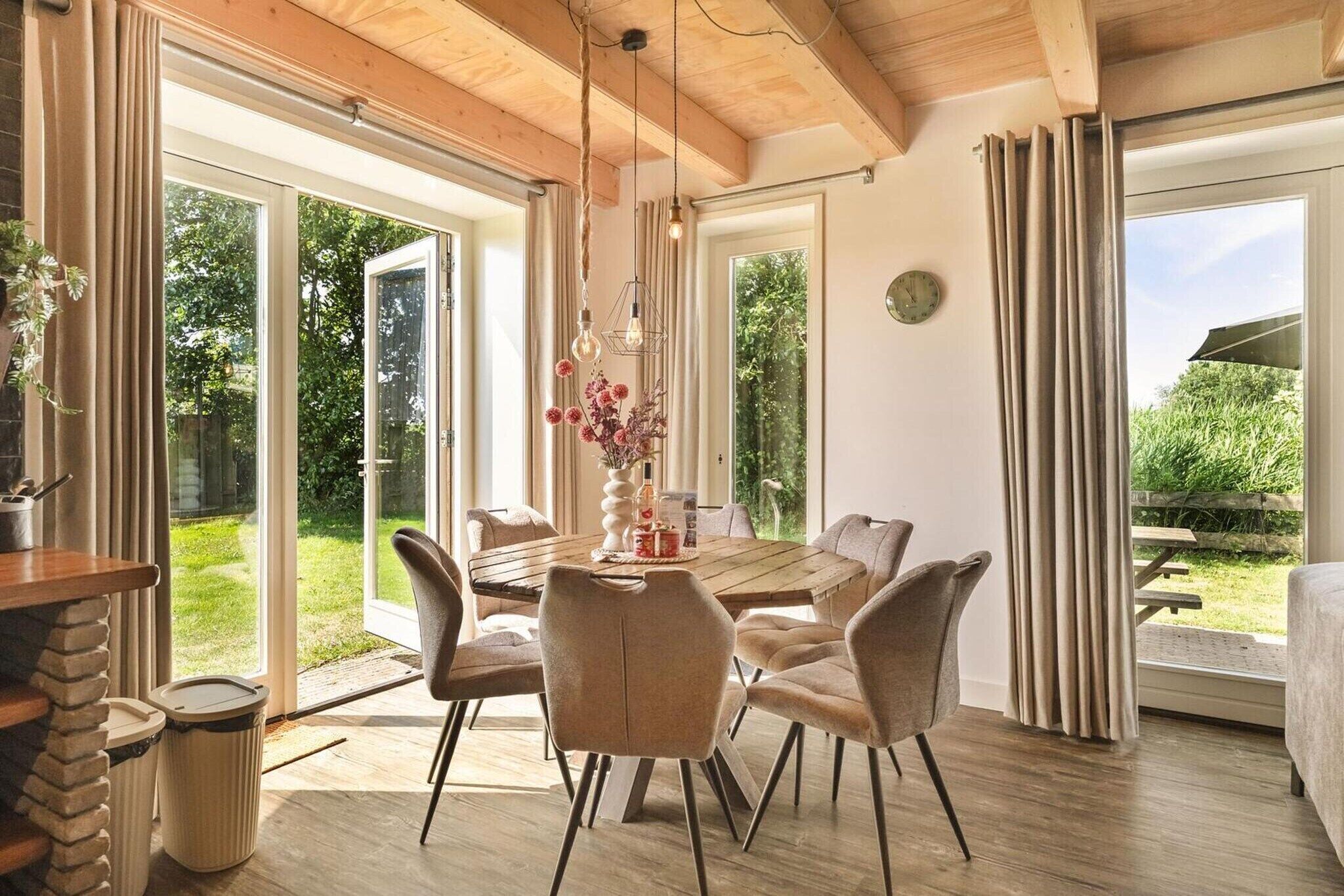 Een eetruimte met een houten tafel en stoelen, een hanglamp en uitzicht op de omgeving.