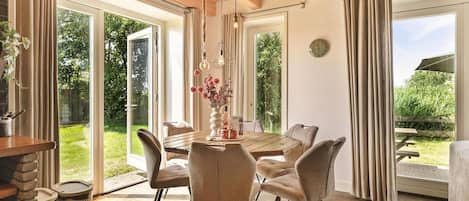 A dining area with a wooden table and chairs, a hanging light fixture, and a view of the outdoors.