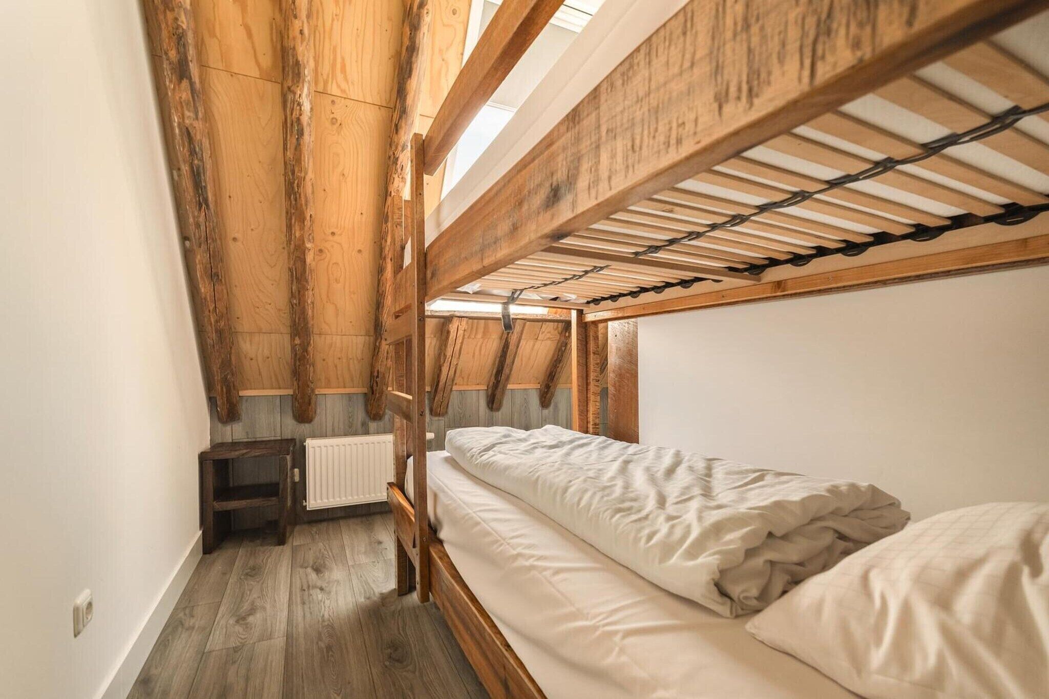 Um quarto pequeno com teto inclinado de madeira, uma cama de solteiro, uma mesa e um radiador.