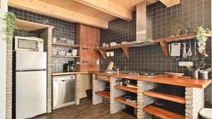 A kitchen with a built-in oven, microwave, and dishwasher, wooden shelves, and a hanging utensil rack. - Vossehoeck 3 Apartment with nature reserve view (Callantsoog)