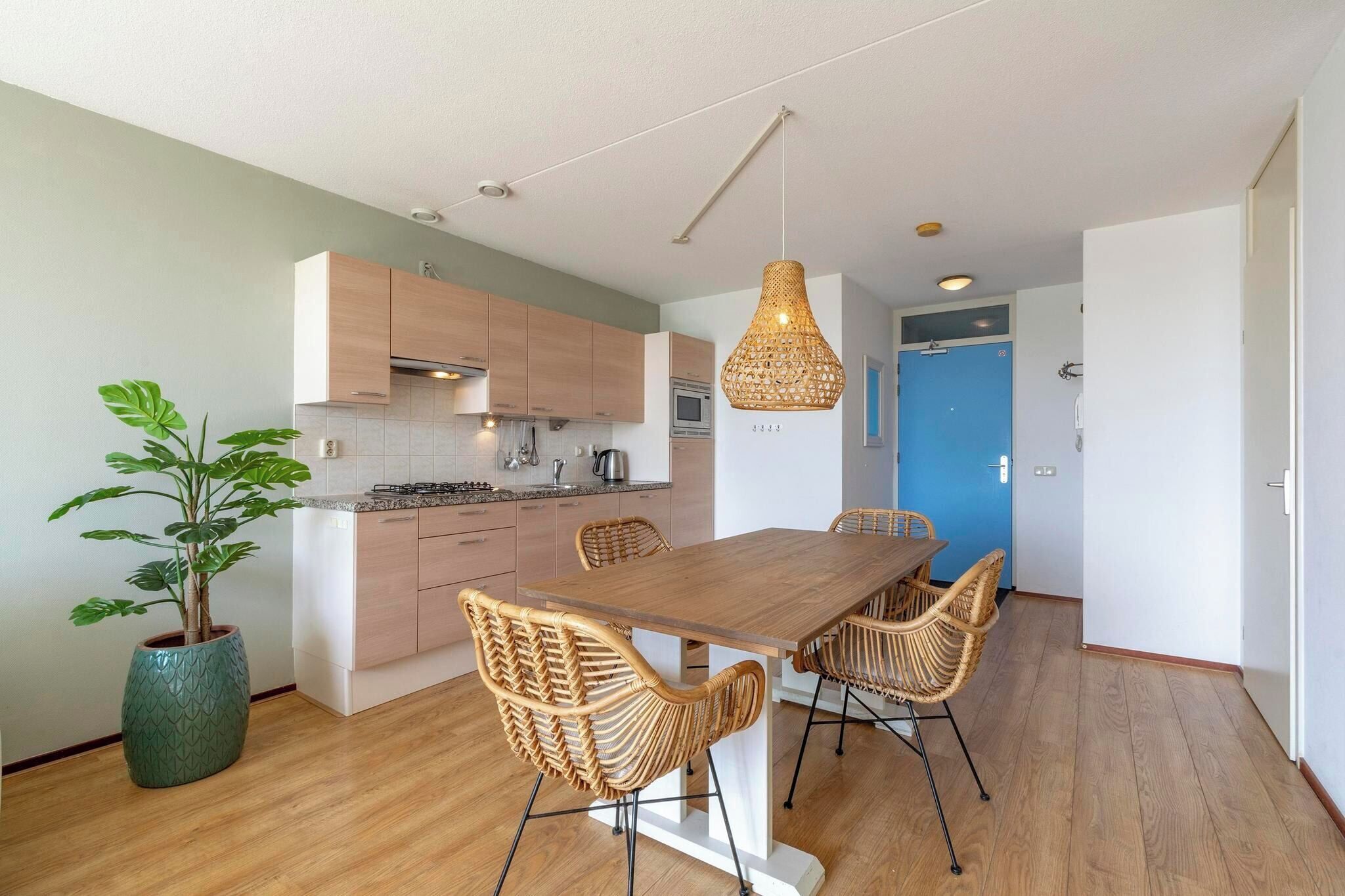 Een moderne keuken met houten kastjes, een eettafel met rieten stoelen en een hanglamp.