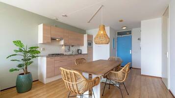 Een moderne keuken met houten kastjes, een eettafel met rieten stoelen en een hanglamp.