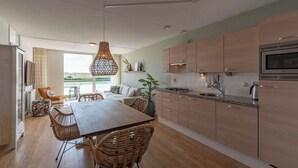 A modern kitchen with wooden cabinets, a dining area with wicker chairs, and a large window overlooking a scenic view. - Apartment in Groote Keeten near the Beach (Groote Keeten)