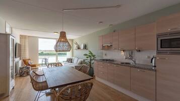 Een moderne keuken met houten kastjes, een eethoek met rieten stoelen en een groot raam met uitzicht op een prachtig landschap.