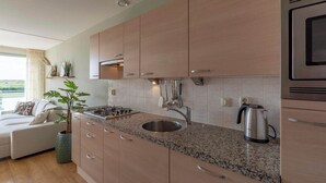 A modern kitchen with granite countertops, stainless steel appliances, and wooden cabinets. - Apartment in Groote Keeten near the Beach (Groote Keeten)