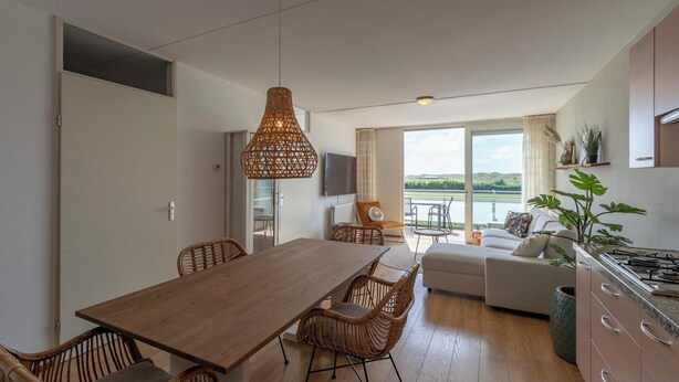 A modern kitchen with a dining area, a sofa, and a view of the outdoors. - Apartment in Groote Keeten near the Beach (Groote Keeten)