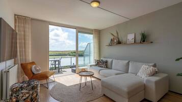 Een moderne woonkamer met een bank, een fauteuil, een klein tafeltje en uitzicht op het omliggende landschap door grote ramen.