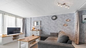 A modern living room with a flat-screen TV, a wooden coffee table, a grey sofa, and a white cabinet.