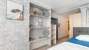 A modern bedroom with a bed, a wardrobe, and shelves with decorative items.