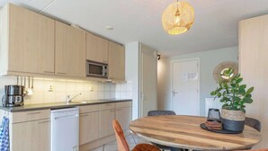 A modern kitchen with wooden cabinets, a microwave, and a dishwasher. There is a dining table with chairs and a hanging light fixture. - Pet-Friendly Apartment (Callantsoog)