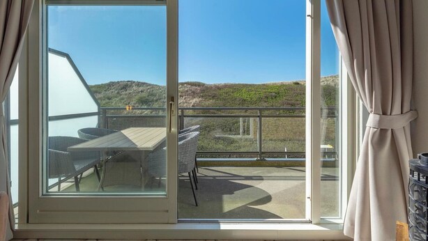 A balcony with a table and chairs, a view of a hilly landscape, and a clear sky. - Pet-Friendly Apartment (Callantsoog)