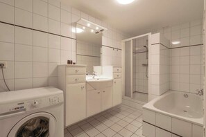 Ein modernes Badezimmer mit Waschmaschine, Waschbecken, Spiegel und Duschkabine.