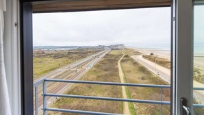 A view from a window overlooking a coastal road with a beach and distant buildings. - Studio Apartment in Seaside with Panoramic Views (Middelkerke)