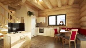 Interior moderno de cabaña de troncos con comedor de madera, cocina y televisor sobre un mueble de madera.