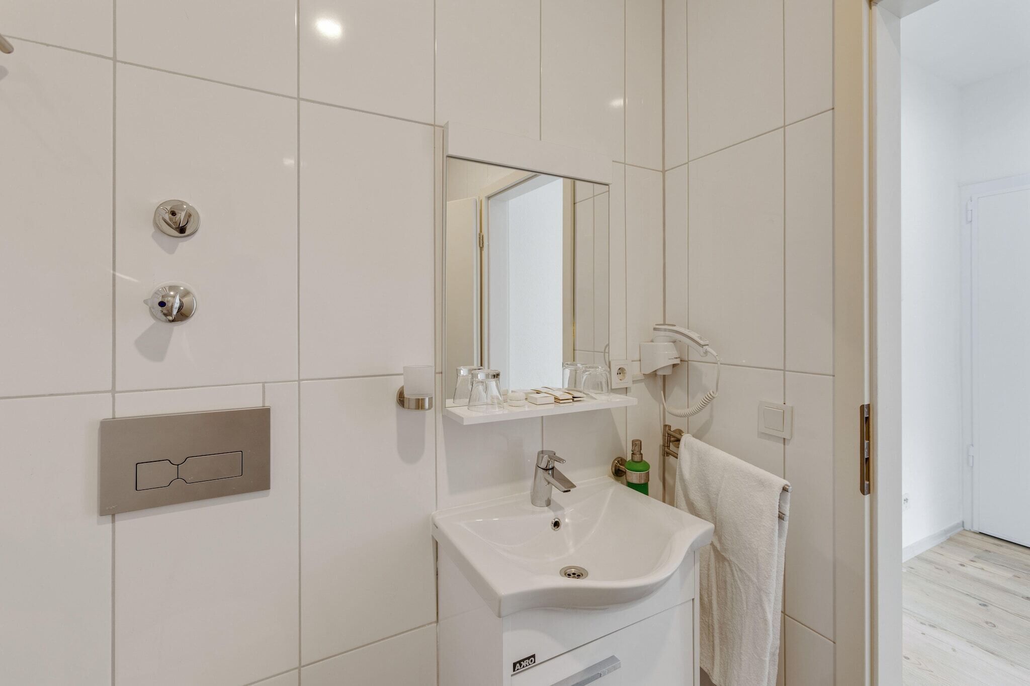 Ein modernes Badezimmer mit weißen Fliesen, einem Waschbecken, einem Spiegel und einem Handtuchhalter.