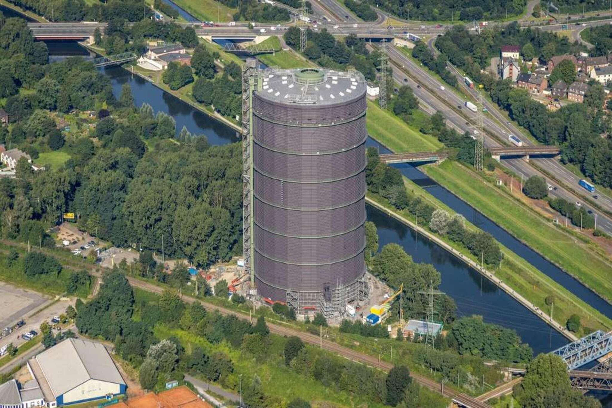 A cylindrical industrial building with a flat roof, surrounded by greenery and a river.