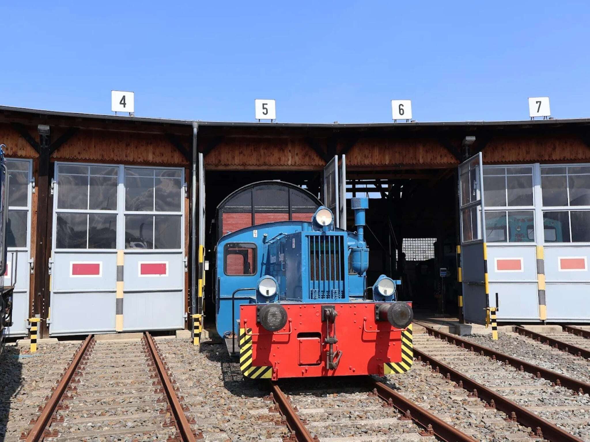 Un treno blu in una stazione ferroviaria, con binari numerati 4, 5, 6 e 7.