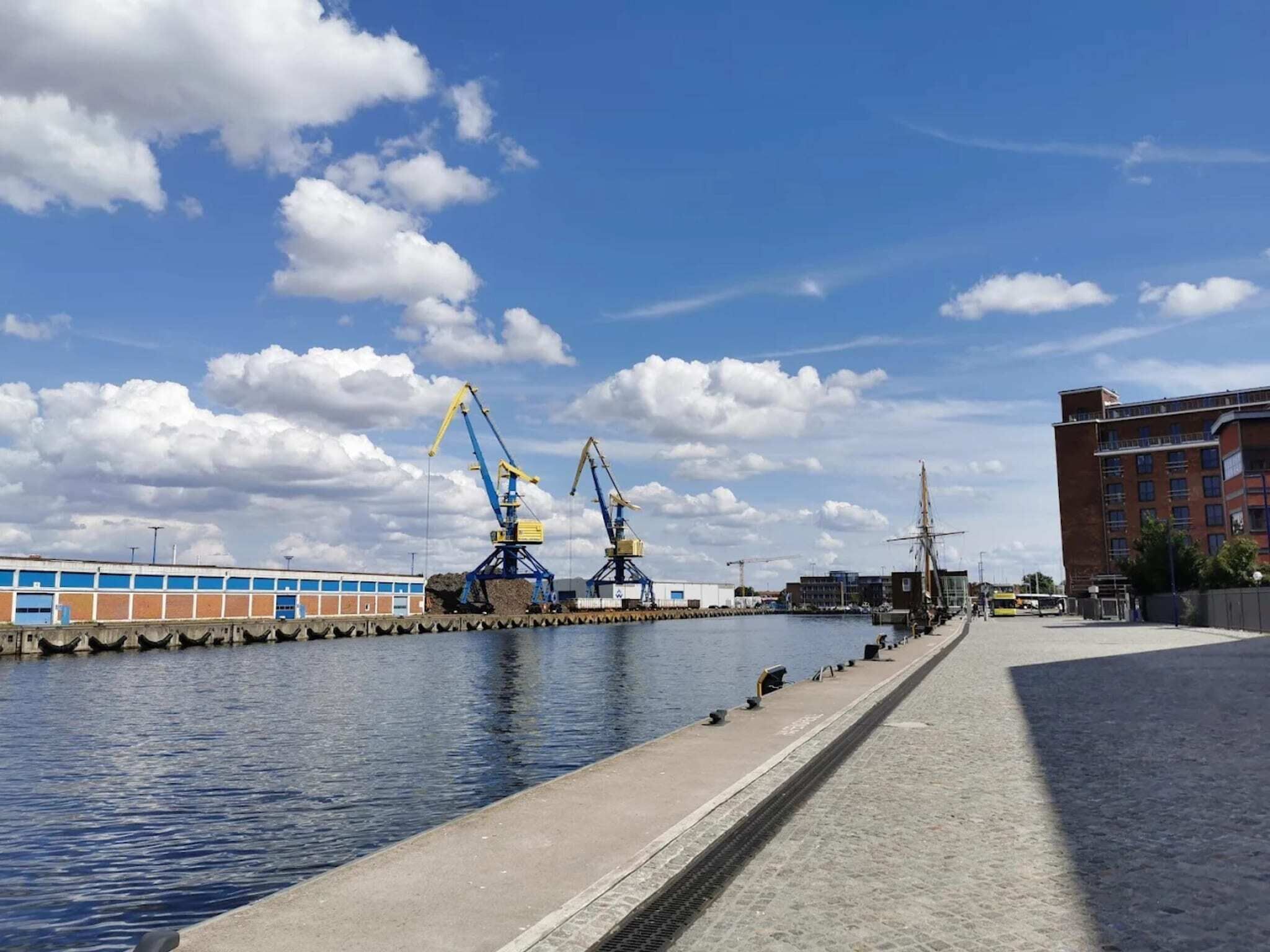 A waterfront area with industrial cranes, a dock, and a building with a flat facade.