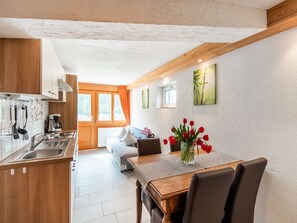 Een moderne keuken met houten kastjes, een eethoek met een tafel en stoelen, en een besneeerd landschap zichtbaar door grote ramen.