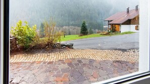 A stone-paved driveway leading to a white house with a red-tiled roof, surrounded by greenery and a mountainous backdrop. - Apartment in Sankt Gallenkirch near Ski Slopes (Vorarlberg)